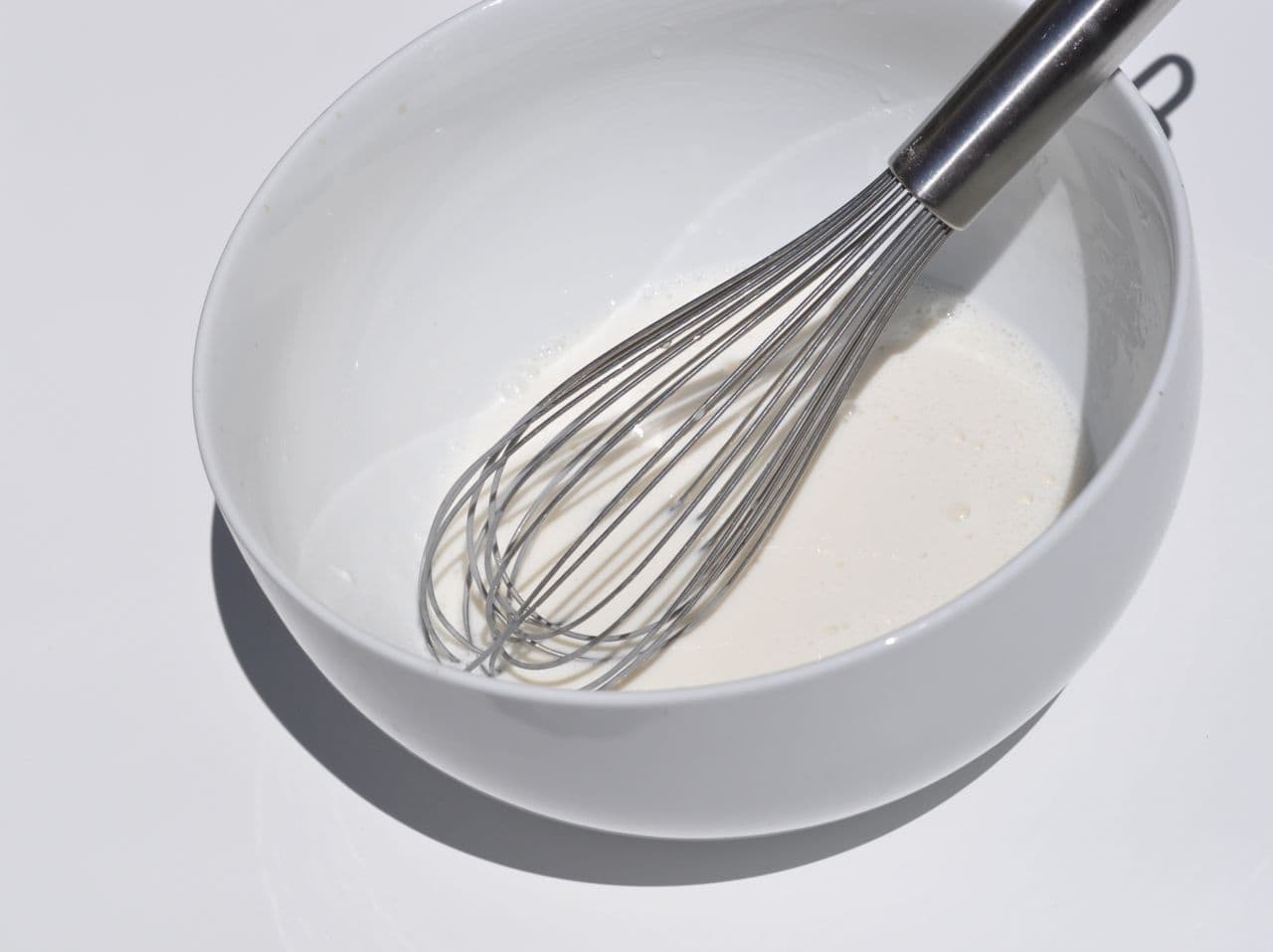wire whisk in white bowl with white liquid inside