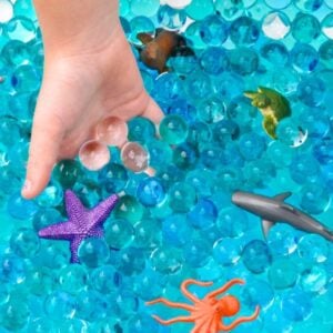blue ocean sensory bin with ocean animals and hand inside