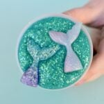 Glitter mermaid slime in plastic container with two mermaid tails