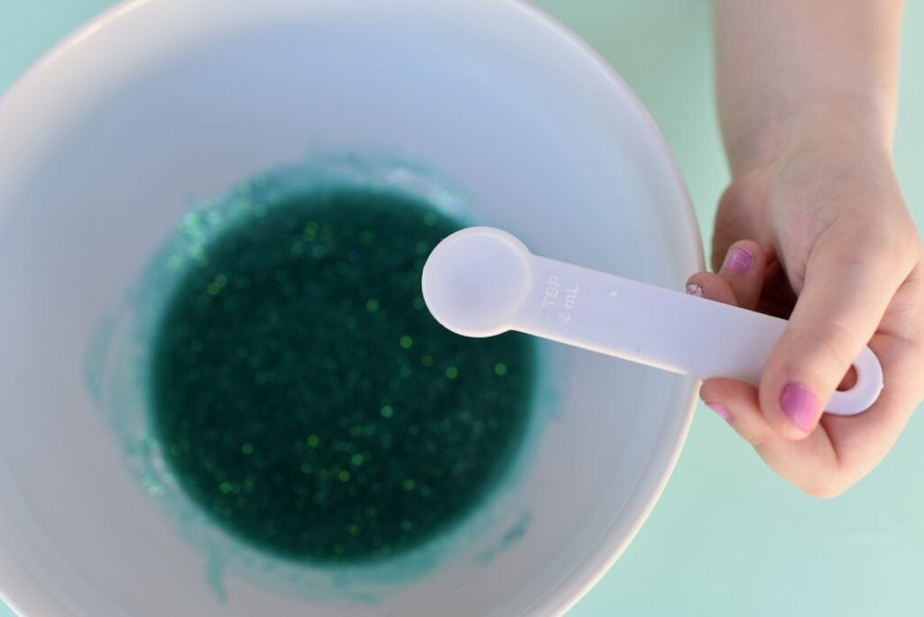 White measuring spoon and mermaid slime mixture