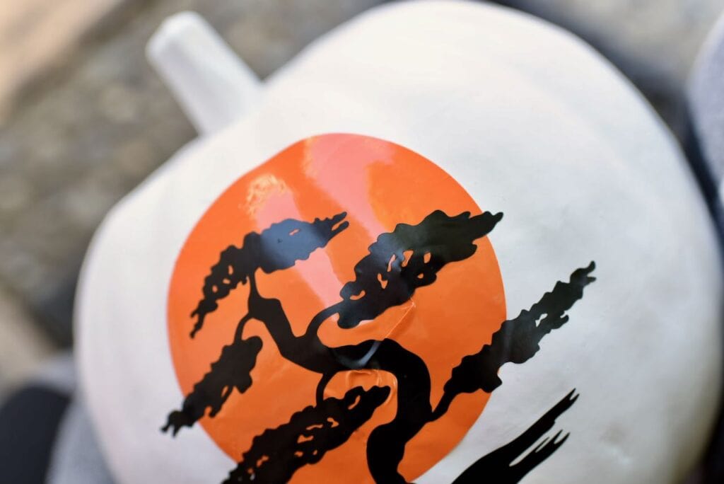 White pumpkin with orange sun and black tree