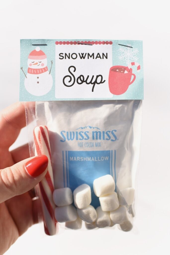 hand holding snowman soup label with hot cocoa, candy cane, and marshmallows inside