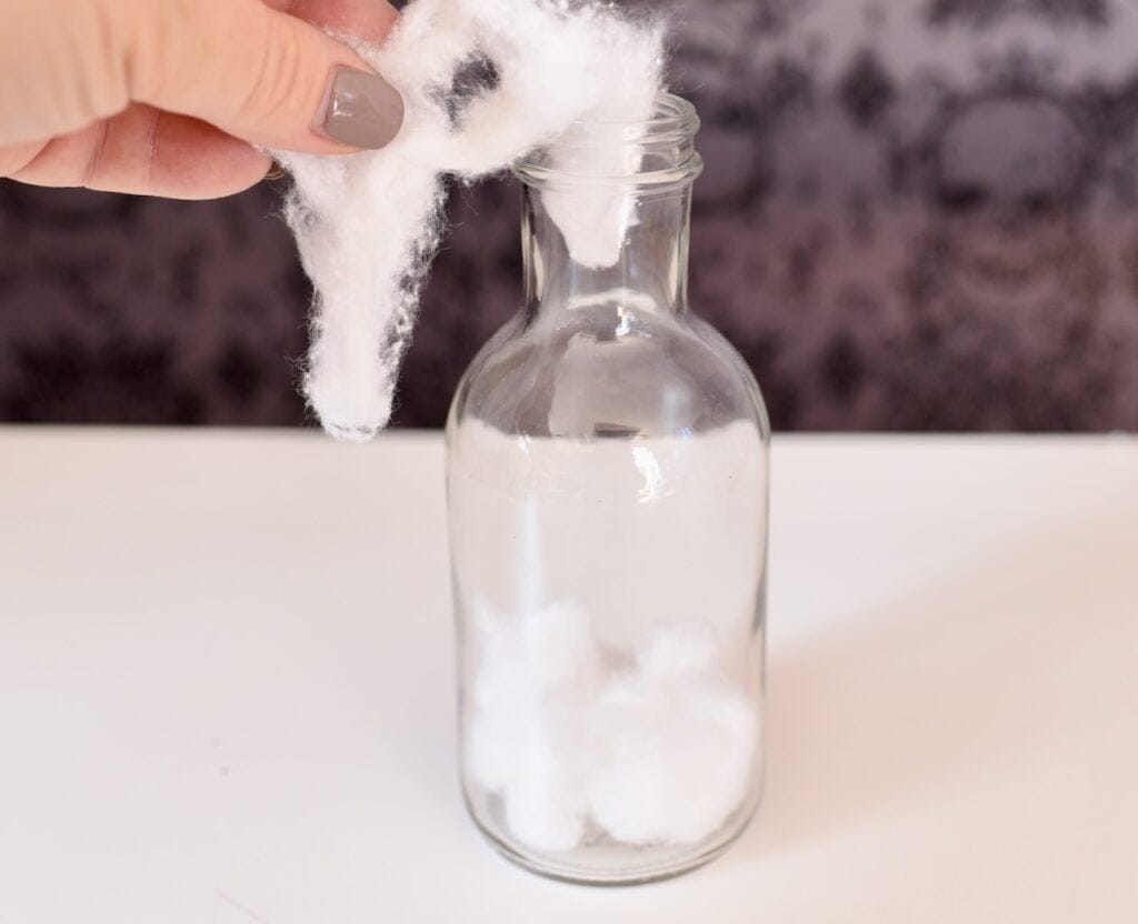 clear glass jar with hand placing cotton balls inside