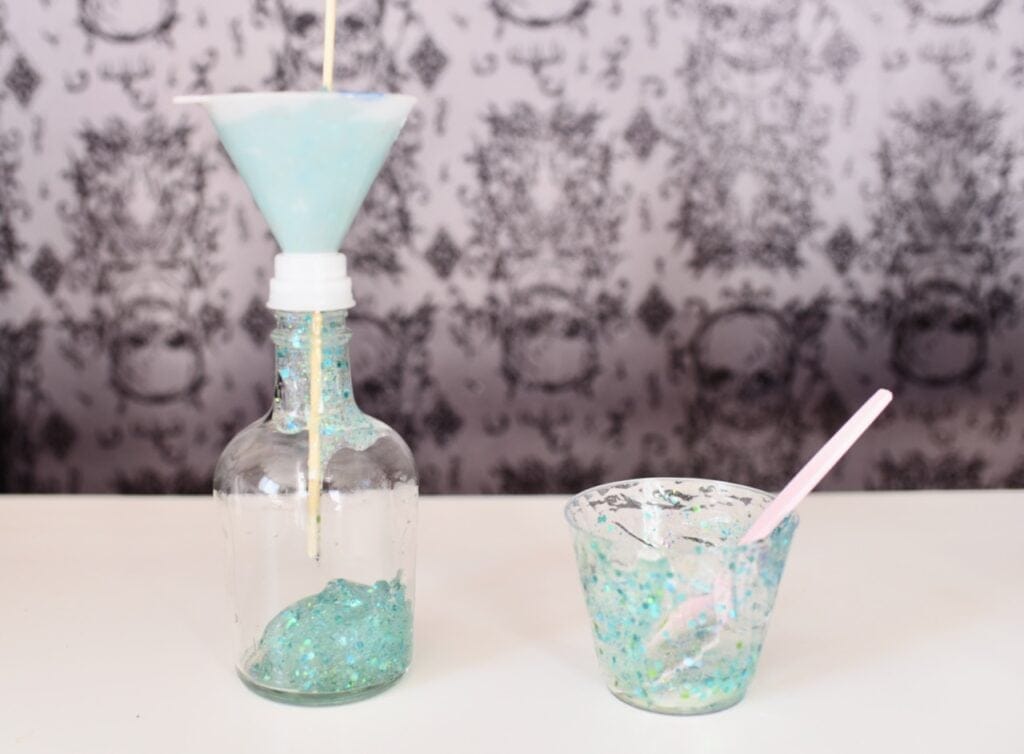 Glass jar with funnel on top next to plastic cup