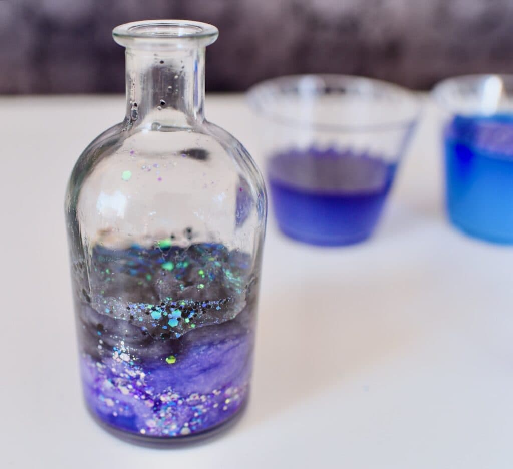 Clear glass jar partially full with purple and blue swirling glitter liquid
