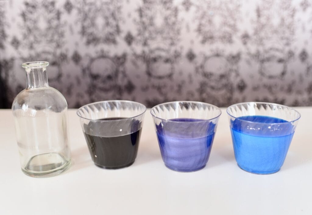 three clear cups with blue, purple, and black paint inside