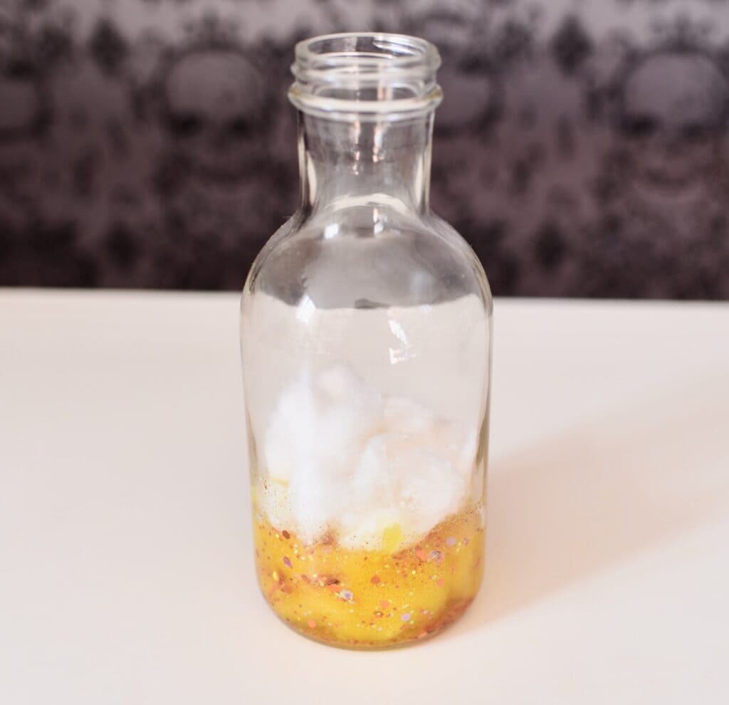 Clear glass bottle with cotton balls and yellow liquid inside