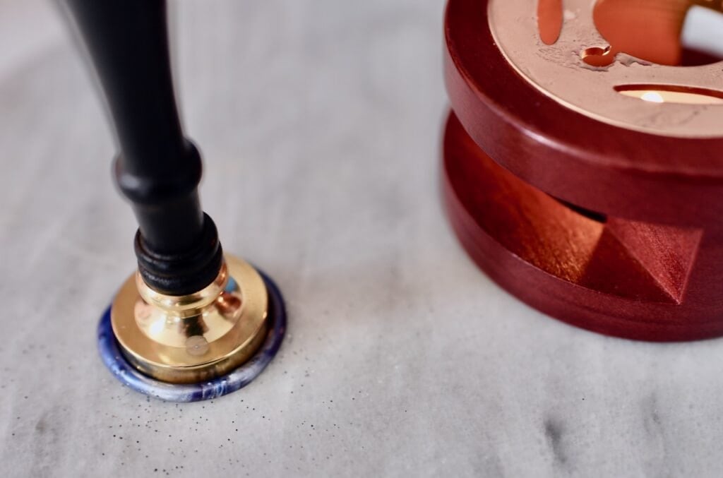 Wax seal pressing into blue and purple wax on marble counter