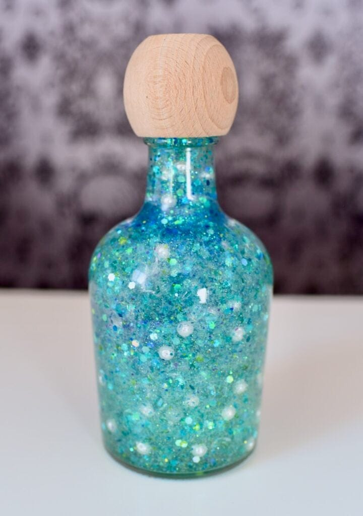 Glass bottle with wood lid with blue glittery liquid inside