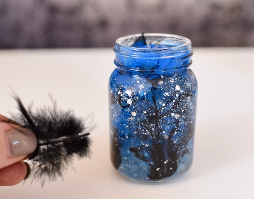 black feathers inside royal blue glittery liquid in glass jar