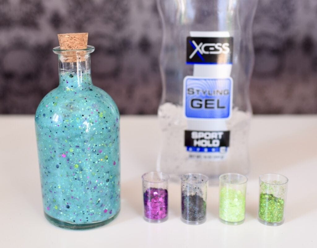 light blue glittery liquid in glass bottle next to glitter bottles