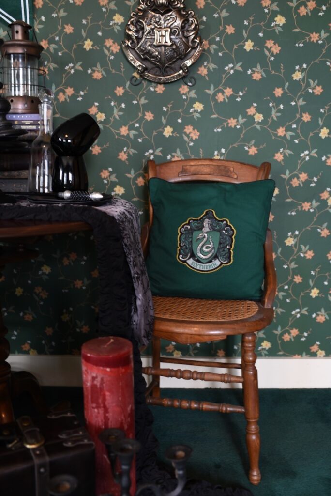room with green wallpaper with wood chair and green Sytherin pillow with snake