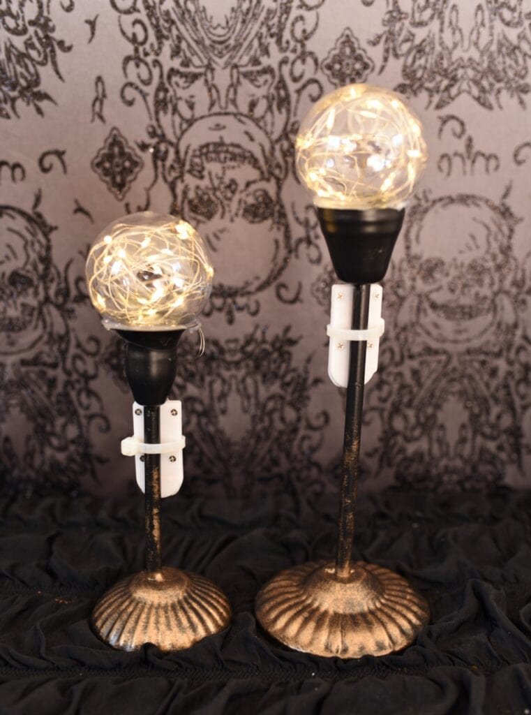 two black candle holders with fairy light in clear bulb on top
