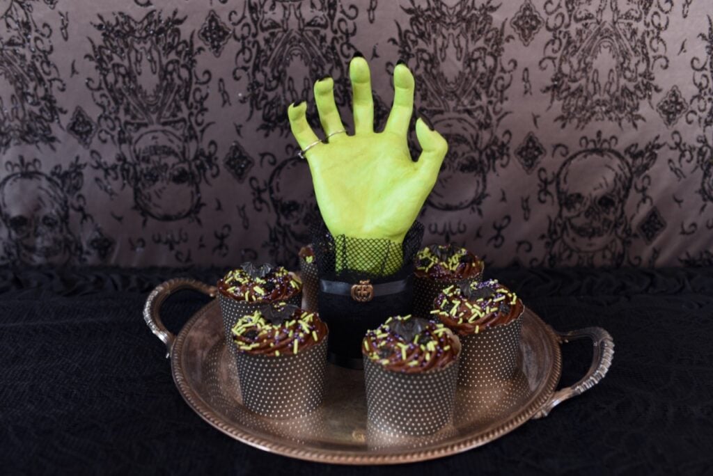 green hand coming out of silver tray with chocolate cupcakes on it